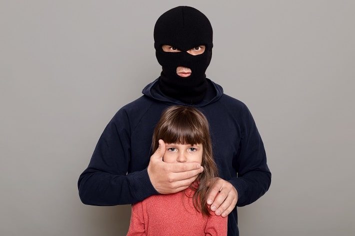 黒のフェイスマスクを付けた男が後ろから少女の口を手で覆い誘拐している様子。